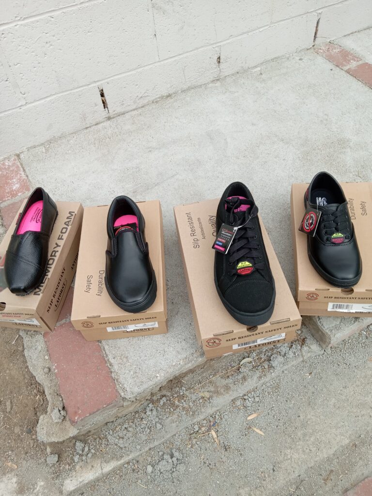Four pairs of black shoes displayed on cardboard boxes outdoors.